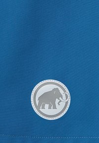 Blauwe stof met een gladde textuur heeft een rond logo met een grijze mammoet, omlijnd met een witte stikseldetail.