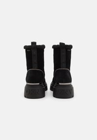 Bottines en suede noires avec un col en fourrure texturée, semelle épaisse noire et logo "DKNY" embossé sur le talon et à l'arrière.