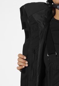 Black insulated jacket featuring a zippered pocket, Velcro accents, and a smooth interior lining. The collar is slightly raised.