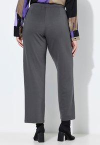 Szare spodnie o szerokich nogawkach wykonane z miękkiego materiału, z elastyczną talią i gładką fakturą, zestawione z czarnymi butami na obcasie.