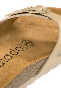 Sandalo beige con cinturino in pelle curvato e fibbia metallica. La soletta è in materiale scamosciato con una superficie testurizzata, etichettata e imbottita.