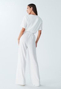 Biały, teksturowany dwuczęściowy strój składający się z luźnej bluzki z krótkim rękawem oraz szerokich spodni z elastycznym pasem.