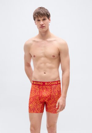 Boxer rouge et orange à motifs avec une ceinture douce portant le nom de la marque "BJÖRN BORG" en jaune. Texture lisse et coupe ajustée.