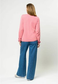 Maglietta rosa a maniche lunghe con scollatura rotonda, abbinata a jeans blu a gamba larga. L'outfit presenta una veste comoda e una texture morbida.