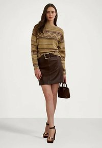 Moteris dėvinti raštuotą smėlio spalvos megztinį, tamsiai rudą odinę sijoną su diržu, laikanti mažą rudą rankinę ir avinti aukštakulnius sandalus.