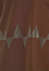 Brunt stof med en ribbet struktur har et metallisk sølv zigzag-mønster hen over midten, hvilket skaber et kontrasterende geometrisk design.