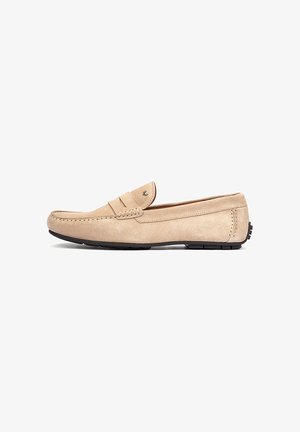 Beige suède loafer met mocassin- stiksel detail en zwarte rubberen zool, zijaanzicht op witte achtergrond.