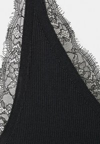 Tissu côtelé noir avec un bord en dentelle florale délicate le long d'un bord en forme de V, montrant un tricot fin et des détails de motif de dentelle complexe.