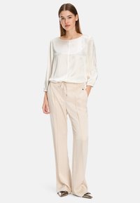 Lightweight satin blouse, cream, with a rounded neckline and long billowy sleeves, paired with beige tailored trousers and metallic heels.