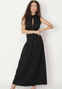 Czarna maxi sukienka z wysokim dekoltem, wycięciem w kształcie łezki z przodu, dopasowaną talią i plisowanym dołem. Gładki materiał i elegancka sylwetka.