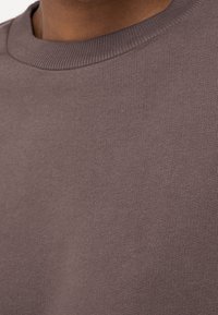 Šedá mikina s kulatým výstřihem vyrobená z měkké látky s hladkou texturou a žebrovaným límcem, s ležérním designem vhodným pro každodenní nošení.