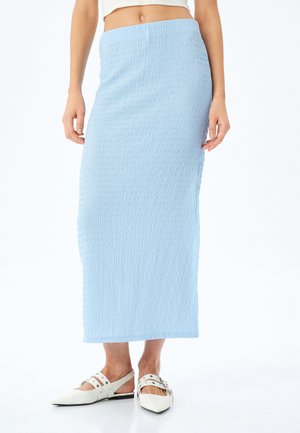 Gonna maxi azzurro chiaro, texturizzata, con una vestibilità aderente e una vita elasticizzata; abbinata a scarpe basse bianche a punta con cinturini e accessori metallici.