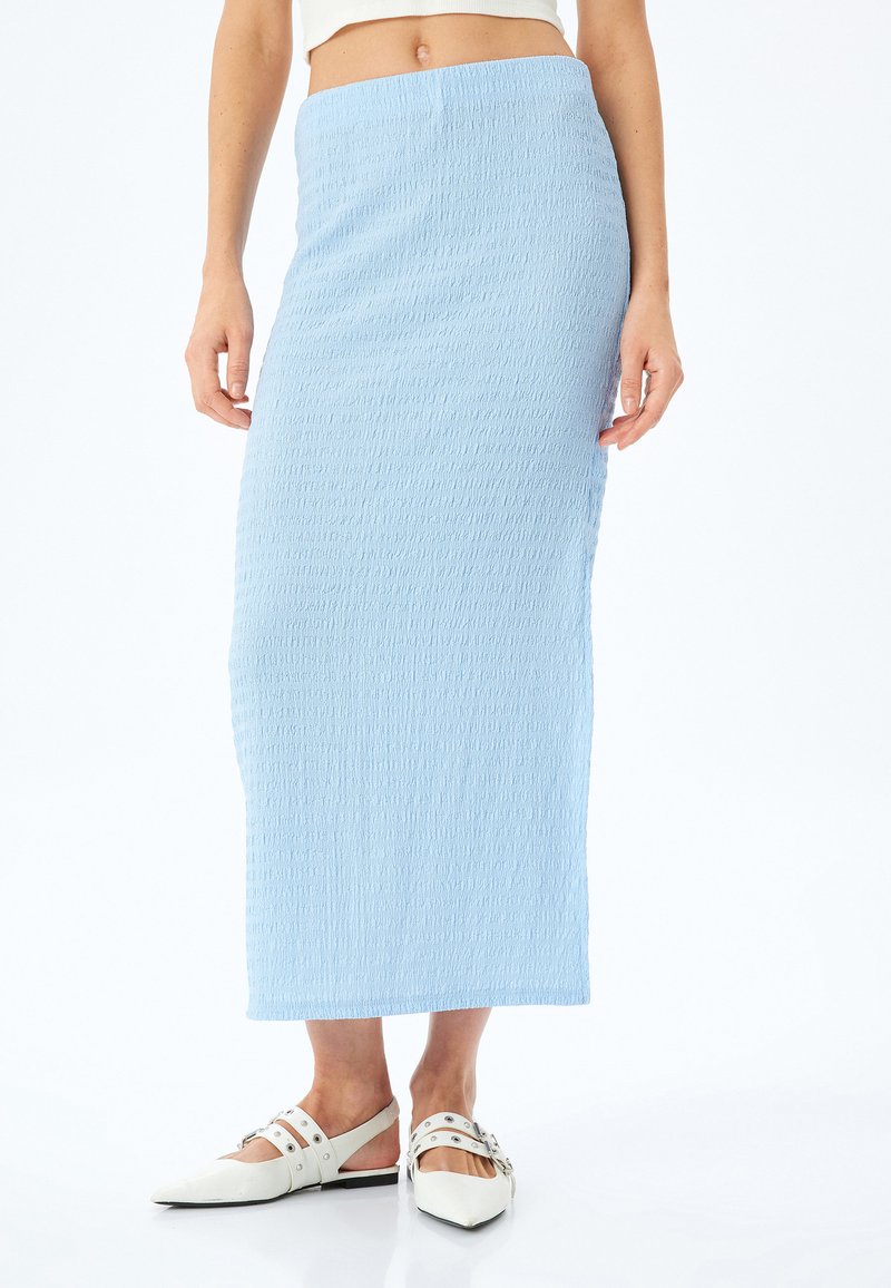 Lichtblauwe, textuur maxi-rok met een slim fit, voorzien van een elastische tailleband; gedragen met witte puntige ballerina's met straps en hardware.