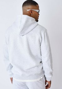 Sudadera de color gris claro hecha de suave material de forro polar. Presenta una capucha con cordones, puños y dobladillo acanalados, con un ajuste holgado y aberturas laterales.