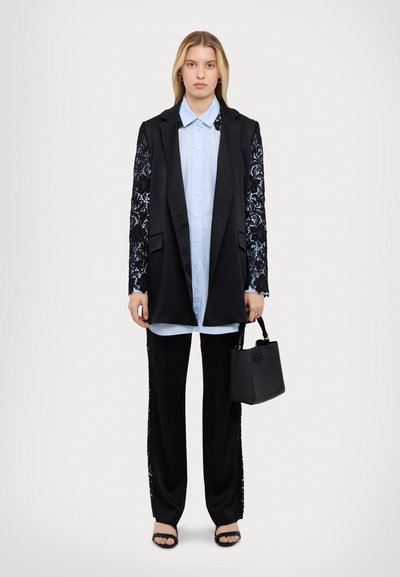 Blazer nero con maniche in pizzo, camicia azzurra chiara, pantaloni neri con dettaglio in pizzo ai lati, borsa nera e sandali neri.