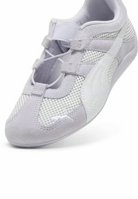 Lys grå sporty sko med mesh og ruskinds-materiale. Har elastiske snørebånd, gummisål og hvide accenter, herunder logo-detaljer.