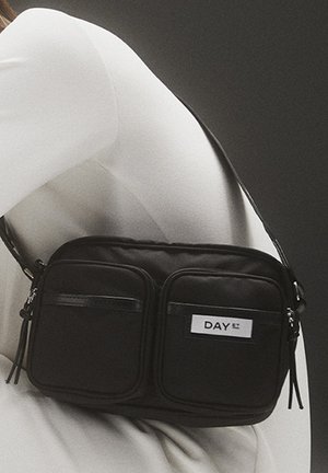 Schwarze Umhängetasche aus Nylon mit zwei vorderen Reißverschlusstaschen, verstellbarem Riemen und einem weißen Etikett mit dem Text "DAY ET."