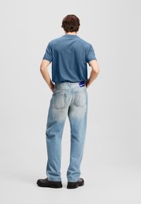 Μπλε βαμβακερό t-shirt με χαλαρή εφαρμογή, σε συνδυασμό με σαχεία τζιν με ελαφρύ πλύσιμο που έχει ξεθωριασμένη υφή και δύο πίσω τσέπες. Μαύρα παπούτσια.