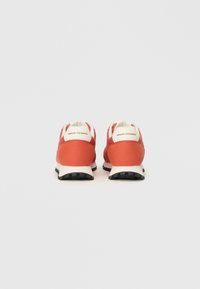 Zapatillas deportivas rojas con una parte superior de textil suave, detalles en blanco y una suela de goma negra con un dibujo texturizado para mayor agarre.