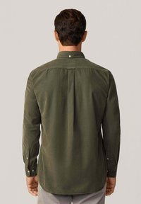 Camisa de algodón verde con cuello abotonado, mangas largas y un pliegue en la parte posterior, que muestra una textura suave y un corte ajustado.