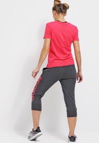 Roze t-shirt met korte mouwen en een ronde hals, gecombineerd met grijze cropped sweatpants met een rood "adidas" logo langs het been.