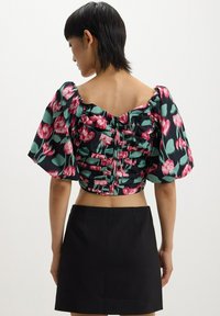 Top corto floreale con un motivo verde e nero decorato con fiori rosa, design a spalle scoperte e dettagli arricciati sul retro. Abbinato a una gonna nera.
