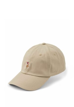 Smilende kvinde med langt blondt hår iført en beige kasket med en polo-spiller logo og en sort zip-up jakke med et matchende broderet logo.