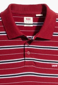 Polo rayé rouge et blanc avec une rayure noire, doté d'un col et de deux boutons. Le patch du logo Levi's est présent sur le côté gauche.