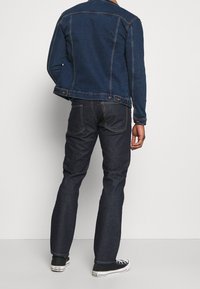 Mörkblå denimjacka med skräddarsydd passform, knapppanel vid midjan, kombinerad med mörka denimjeans och svarta sneakers.