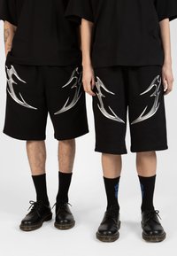 Black shorts with silver flame-like designs on the sides, paired with black shoes and socks, featuring blue graphic accents.