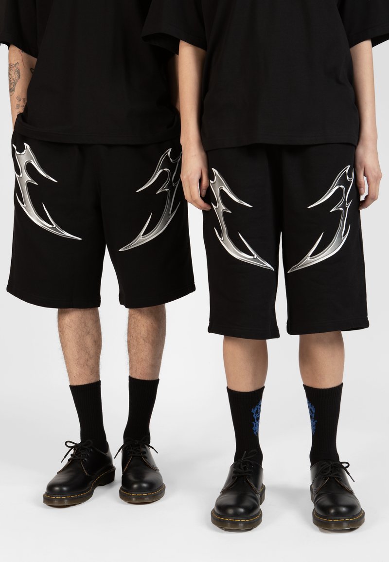 Black shorts with silver flame-like designs on the sides, paired with black shoes and socks, featuring blue graphic accents.