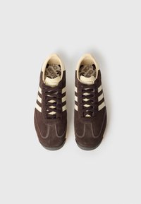 Braune Wildledersneaker mit cremefarbenen Streifen, strukturierten Schnürsenkeln und einer Gummisohle. Sie verfügen über ein gepolstertes Innenfutter und eine gemusterte Innensohle.