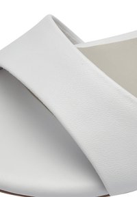Vita lädersandaler med en böjd tvärremdesign, slät yta och en minimalistisk estetik. Sålen är neutral i färgen.