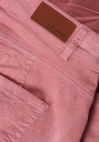Roze corduroy stof met zichtbare ribbeltextuur, voorzien van een leren label met de opdruk "TNTUUM" en een zijzakdetail.