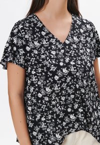 Sort kortærmet top med V-halsdesign og et hvidt blomstermønster, lavet af letvægtsstof med en afslappet pasform.