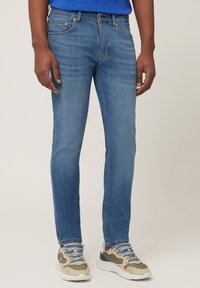 Light blue denim jeans with a slim fit, five pockets, and copper hardware. Paired with neutral-toned athletic shoes featuring blue laces.