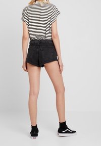 Svarta högmidjade denimshorts med fransad fåll, matchade med en svart och vit randig kortärmad skjorta och svarta sneakers.