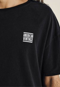 Juodas medvilnės marškinėliai su baltu "AMERICAN VINTAGE" logotipu ant krūtinės, apvaliu iškirpimu ir trumpomis rankovėmis. Minkšta tekstūra.
