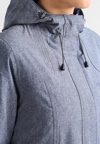 Chaqueta azul texturizada con capucha, que cuenta con cordones ajustables y un diseño estilizado. Incluye detalles de cremallera y bolsillos laterales.