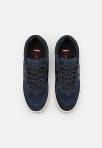 Navy suede sneakers with black stripes, patterned laces, and a white rubber sole. Features padded collar and embossed logo details.