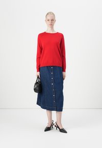 Red knit sweater, denim midi skirt with button details, black handbag, and black pointed-toe heels. Plain background enhances focus.