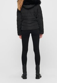 Svart vadderad jacka med en huva foder av päls, med en quiltad design. Bärs med svarta, åtsittande byxor och svarta ankelstövlar.