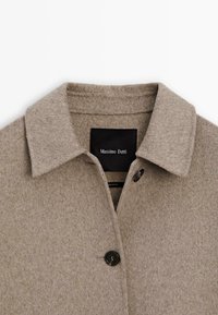 Beige wollen jas met een kraag, enkele knoopsluiting en een zwart label met "Massimo Dutti" in de kraag.