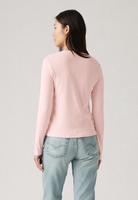 Lichtroze longsleeve top met een ronde hals, aansluitend design en zachte textuur, gecombineerd met lichtblauwe denim jeans.