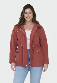 Giacca rossa con zip, vita regolabile con coulisse, due tasche anteriori e cappuccio. Realizzata in materiale leggero con una texture liscia.