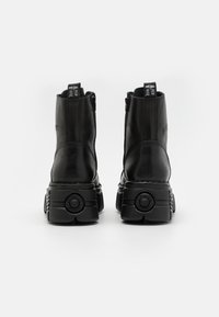 Bottines noires en cuir avec une semelle épaisse, un talon rembourré et un détail de fermeture éclair décoratif. Présente un logo à l'arrière.