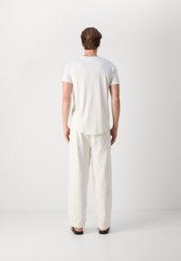 Vit t-shirt med kort ärm och löst sittande vita byxor, båda med en slät textur, avslappnad passform och minimalistisk design.