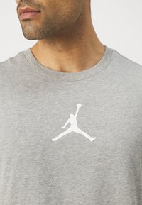 Grå bomulls t-skjorte med hvit Jordan-logo trykk på brystet, med rund halslinning og korte ermer. Glatt tekstur.