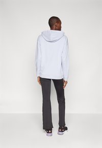 Lyseblå hoodie med snoretræk i hætten, parret med mørkegrå tætsiddende bukser og sorte sportssko med lyserøde detaljer. Glat stofstruktur.
