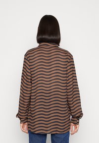 Camicia a maniche lunghe in marrone e blu navy con un motivo a strisce ondulate, realizzata in un tessuto liscio. Presenta un colletto e polsini con bottoni.